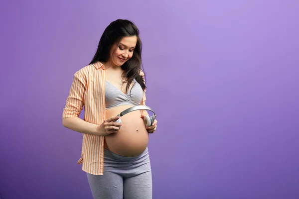 Mujer embarazada pone auriculares en el abdomen para que su bebé escuche los sonidos de la naturaleza — Foto de Stock
