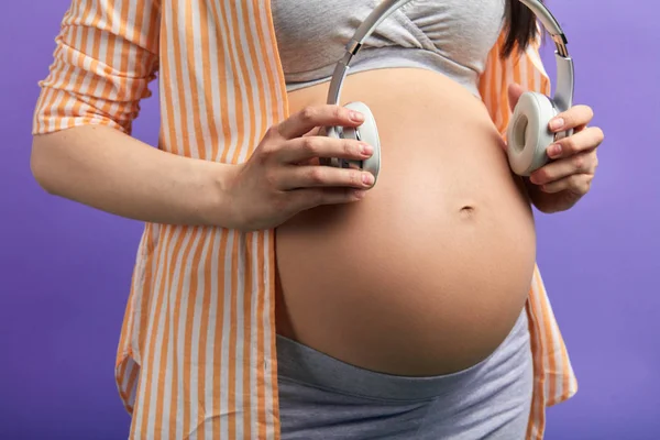Mujer embarazada pone auriculares en el abdomen para que su bebé escuche los sonidos de la naturaleza — Foto de Stock
