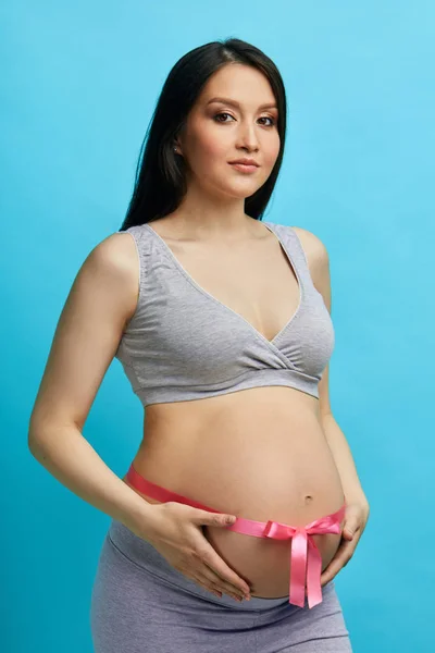 Przycięty obraz pięknej kobiety w ciąży przytulającej swój brzuch różową wstążką — Zdjęcie stockowe
