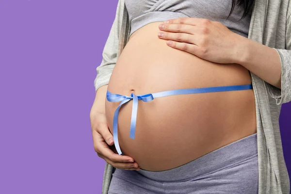 Image recadrée d'une belle femme enceinte embrassant son ventre avec un ruban bleu — Photo