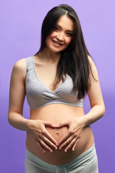 Liebevolle schwangere Frau blickt in die Kamera, während sie im Studio über lila posiert — Stockfoto