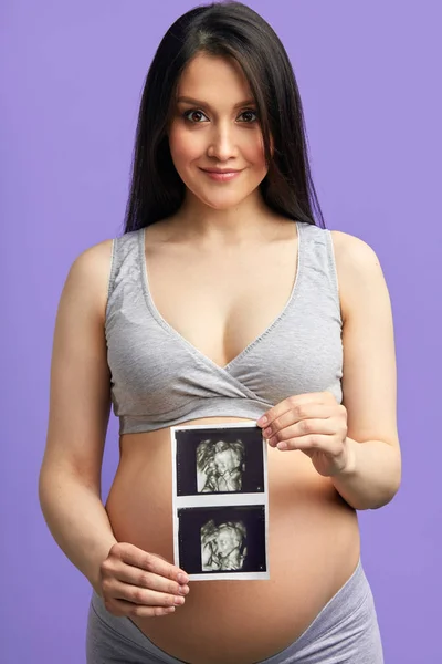 Femeie gravidă care transmite cu bucurie ține scanarea cu ultrasunete în fața burții rotunde — Fotografie, imagine de stoc