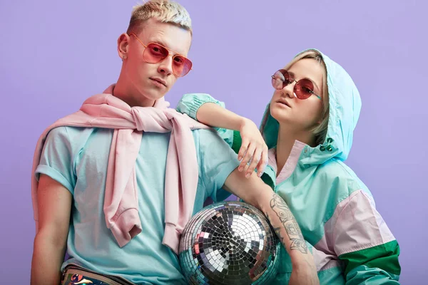 Jovem casal de dançarinos da moda posando com bola de discoteca no fundo violeta — Fotografia de Stock