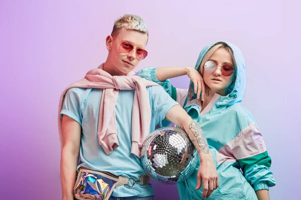 Jovem casal de dançarinos da moda posando com bola de discoteca no fundo violeta — Fotografia de Stock