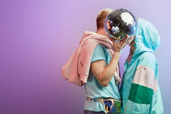 Unga fashionabla par dansare poserar med disco boll på violett bakgrund — Stockfoto