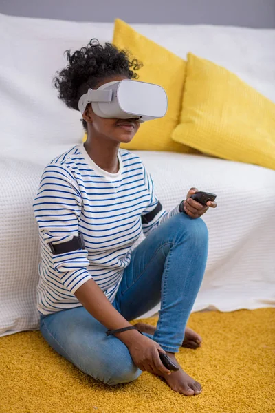 Mujer africana viendo vídeo usando gafas VR con control remoto en casa . —  Fotos de Stock