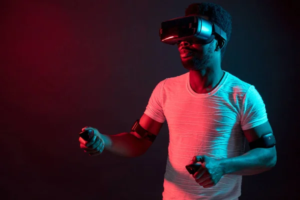 Young man wearing VR headset watching video, isolated on dark red dual light.