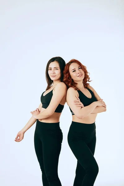 Two caucasian women are stand together in black tank tops and leggings on white — Stock Photo, Image