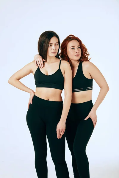 Two caucasian women are stand together in black tank tops and leggings on white — Stock Photo, Image