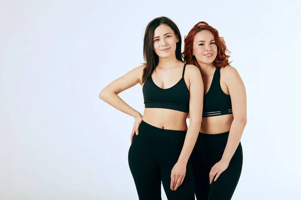 Two caucasian women standing together in black tank tops and leggings on white — Stock Photo, Image