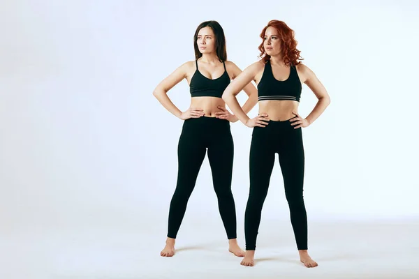 Two caucasian women are stand together in black tank tops and leggings on white — Stock Photo, Image