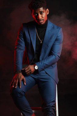 Young dark-skinned entrepreneur in formal clothing, standing against dark wall