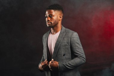 Young dark-skinned entrepreneur in formal clothing, standing against dark wall