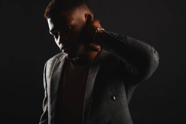 Young dark-skinned entrepreneur in formal clothing, standing against dark wall