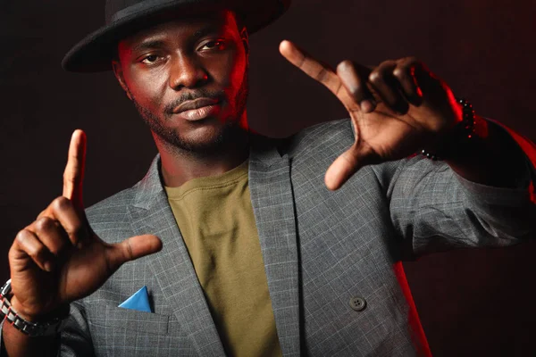 Hombre de negocios africano en traje gris y sombrero negro en estudio sobre fondo oscuro — Foto de Stock