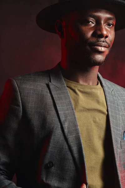 Hombre de negocios africano en traje gris y sombrero negro en estudio sobre fondo oscuro — Foto de Stock
