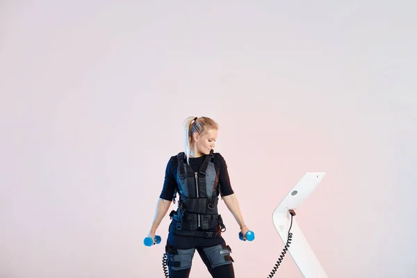 아령과 운동하는 동안 EMS 기계를 확인하는 건강한 소녀 — 스톡 사진