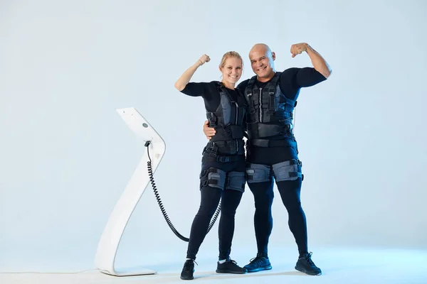 Positive powerful couple in EMS suits with raised arms looking at the camera — Stock Photo, Image