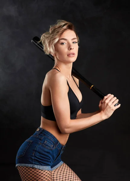 Sexy chica posando sobre un fondo negro con un bate de béisbol en sus manos —  Fotos de Stock