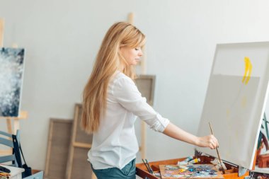 Sarı saçlı kadın fırçayla resim yapıyor.