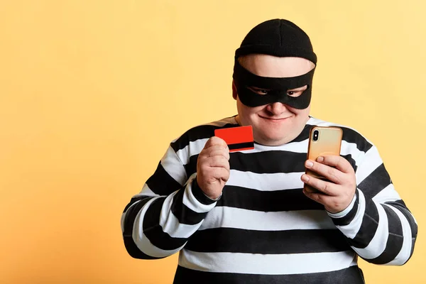 Ευτυχισμένο χαρούμενο παχουλό χάκερ με μια τραπεζική κάρτα και το κινητό τηλέφωνο — Φωτογραφία Αρχείου