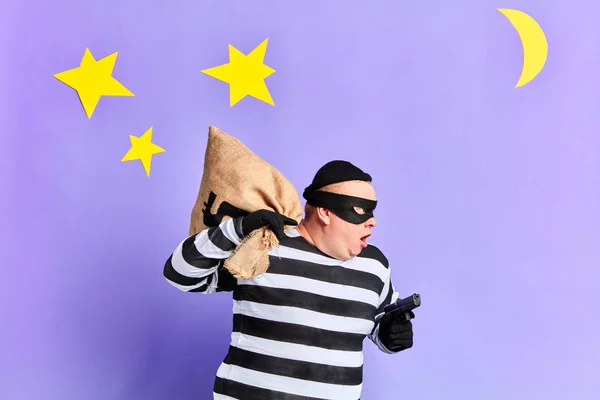 Gefangener in gestreifter Uniform, der ein Verbrechen begeht. Nahaufnahme Seitenansicht Foto. isolierter blauer Hintergrund mit Mond und Sternen. Studioaufnahme. — Stockbild Gefangener in gestreifter Uniform begeht ein Verbrechen — Stockfoto