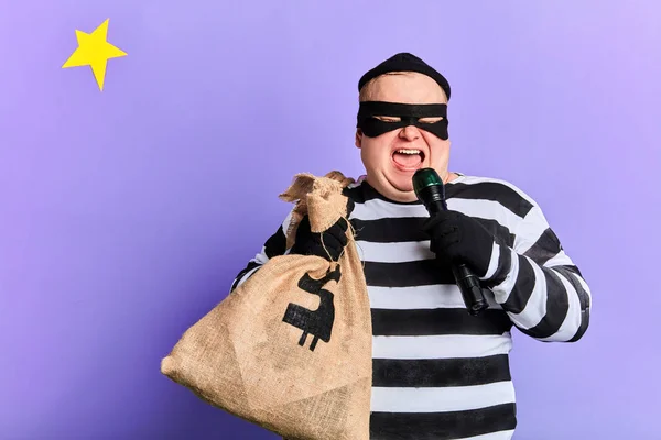 Divertido ladrón regordete con un saco sosteniendo una antorcha y usarlo como micrófono —  Fotos de Stock