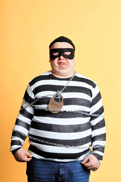 Trauriger emotionaler Gefangener in Maske mit Kette um den Körper, der vor gelbem Hintergrund steht. Studioaufnahmen. Porträt aus nächster Nähe — Stockbild Gefangener in Maske mit Kette um den Körper vor gelbem Hintergrund. — Stockfoto
