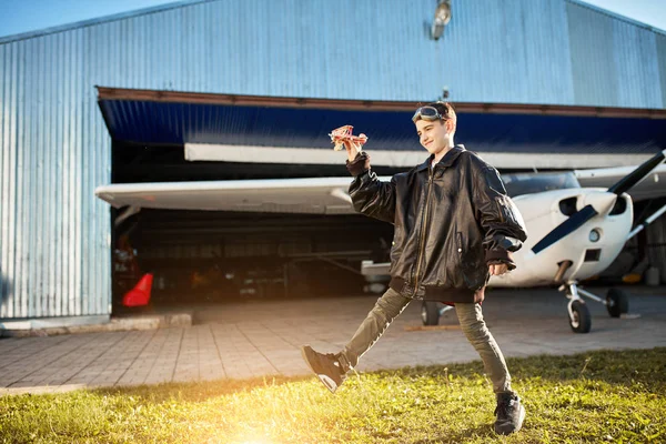Divertido niño sueña con ser un piloto, jugando con el avión de juguete, hangar exterior — Foto de Stock