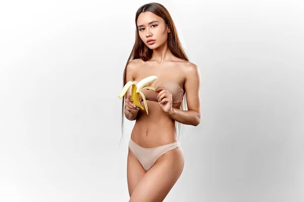 Dünnes, angenehmes Mädchen mit langen dunklen Haaren und einer Banane, die vor der Kamera posiert — Stockfoto