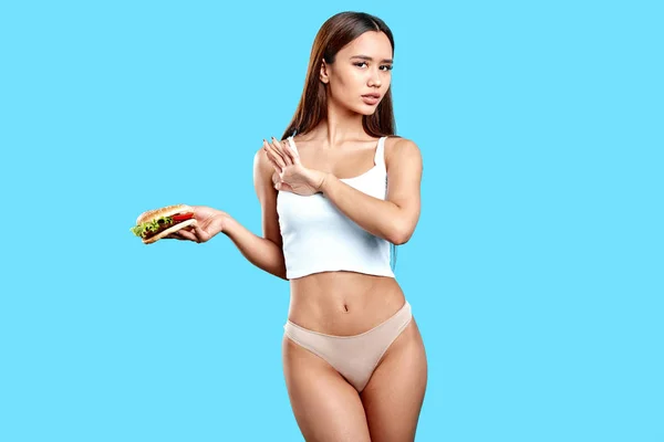 Delgada chica sexy sosteniendo hamburguesa, no quiere comerlo ya que tiene muchas callosidades —  Fotos de Stock