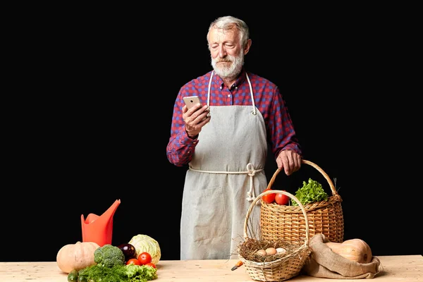 Senior aldeia homem mensagem de texto no smartphone, vai cozinhar jantar saudável — Fotografia de Stock