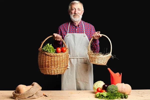 Campesino de pelo gris parado sosteniendo cestas con verduras frescas y huevos — Foto de Stock