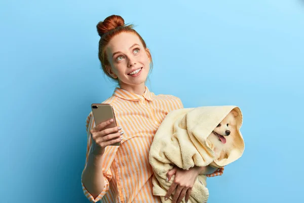 Atractiva chica pensativa mirando hacia arriba, sosteniendo un perro, teléfono móvil — Foto de Stock