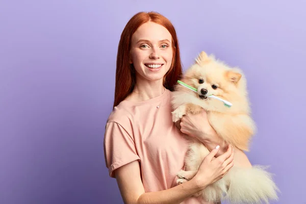 Alegre menina bonita feliz segurando um cão com uma escova de dentes em seus dentes — Fotografia de Stock