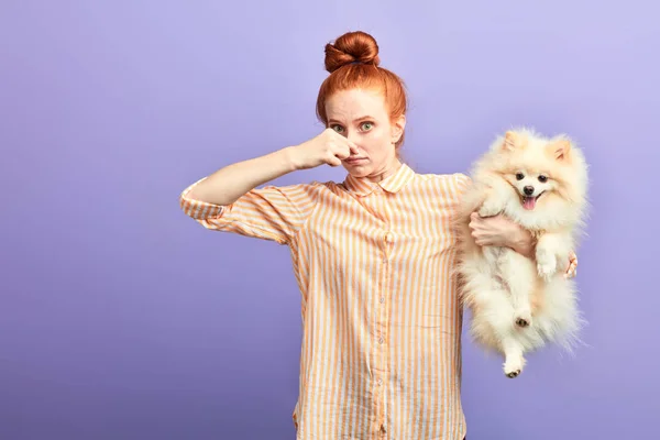 Смешная девушка в стильной полосатой рубашке закрывает нос, так как собака пукает — стоковое фото