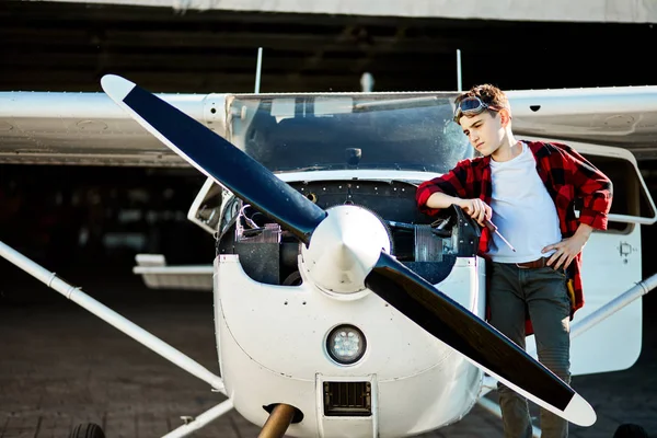 Boy stands outside hangar, near light airplane, dreams to be aircraft engineer — Stock Photo, Image