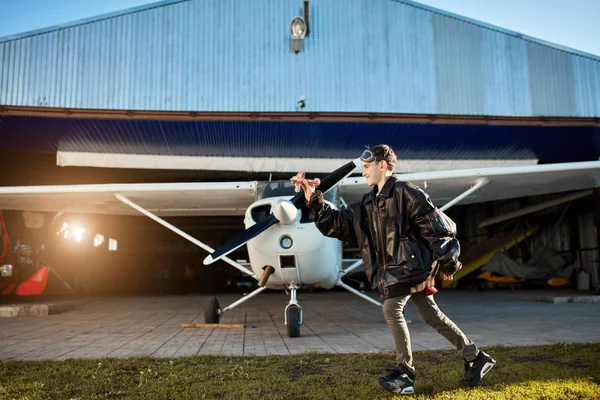 Vista de niño en gafas de aviador jugando con pequeño avión de juguete hecho a mano cerca del aeródromo — Foto de Stock