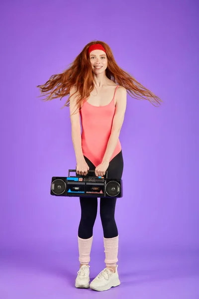 Счастливая студентка с длинными вьющимися рыжими волосами танцует с портативным ретро кассетным проигрывателем — стоковое фото