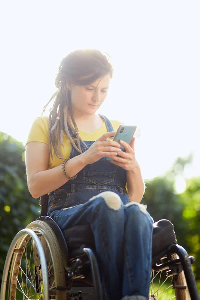 Chica navegando por la red, navegando por Internet mientras está sentado en la silla de ruedas — Foto de Stock