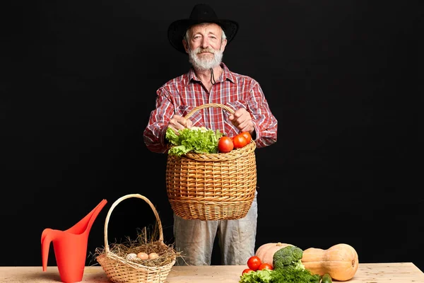 Granjero canoso de pie con una gran cesta llena de lechuga y brócoli en las manos — Foto de Stock