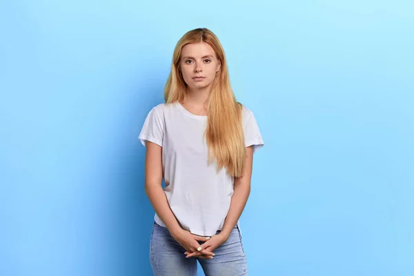 Ξανθιά κορίτσι φορώντας λευκό t-shirt, Τζιν θέτοντας στην κάμερα απομονωμένο μπλε τοίχο — Φωτογραφία Αρχείου