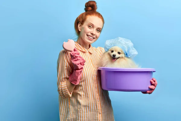 Fille positive tenant un bassin avec un chien et une brosse à cheveux et regardant la caméra — Photo