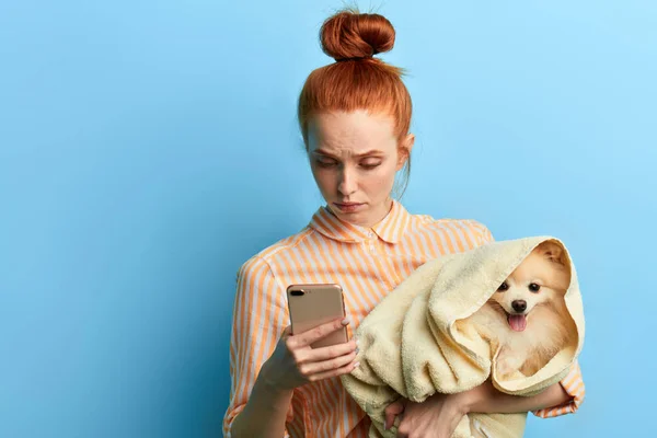 red-haired woman holding a towel with a dog and making a phone call