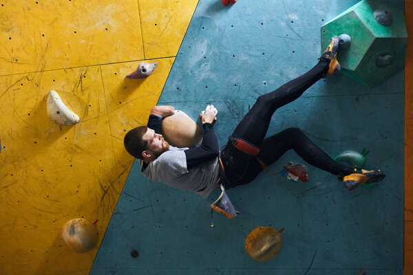 Motivated physically challenged boulderer with beard hanging at climbing wall