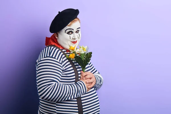 Ρομαντικός ωραίος κλόουν με λουλούδια κοιτάζοντας την κάμερα με την έκφραση του διαγωνισμού — Φωτογραφία Αρχείου