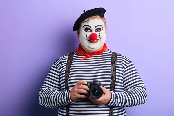 Uśmiechnięty zabawny clown w stiped sweter trzymając aparat fotograficzny — Zdjęcie stockowe