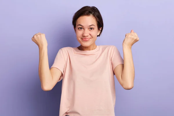 Alegre mujer joven positiva levantando los puños con expresión sonriente encantada —  Fotos de Stock