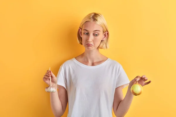 Προβληματισμένος γυναίκα διστάζει τι να χρησιμοποιήσει σκόρδο ή κρεμμύδι — Φωτογραφία Αρχείου