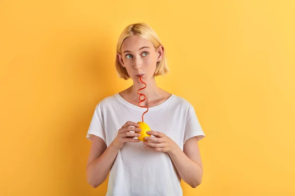 Pretty joyful young woman holding lemon and trying to drink juice from it — Stock Photo, Image